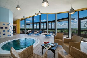 A spacious indoor pool area with lounge chairs and a small table, large windows offering a view of the outdoors. - La Chataigneraie (Maurs)