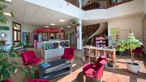 Un hall d’entrée spacieux avec un coin salon rouge, une table centrale et un escalier menant à un niveau supérieur.