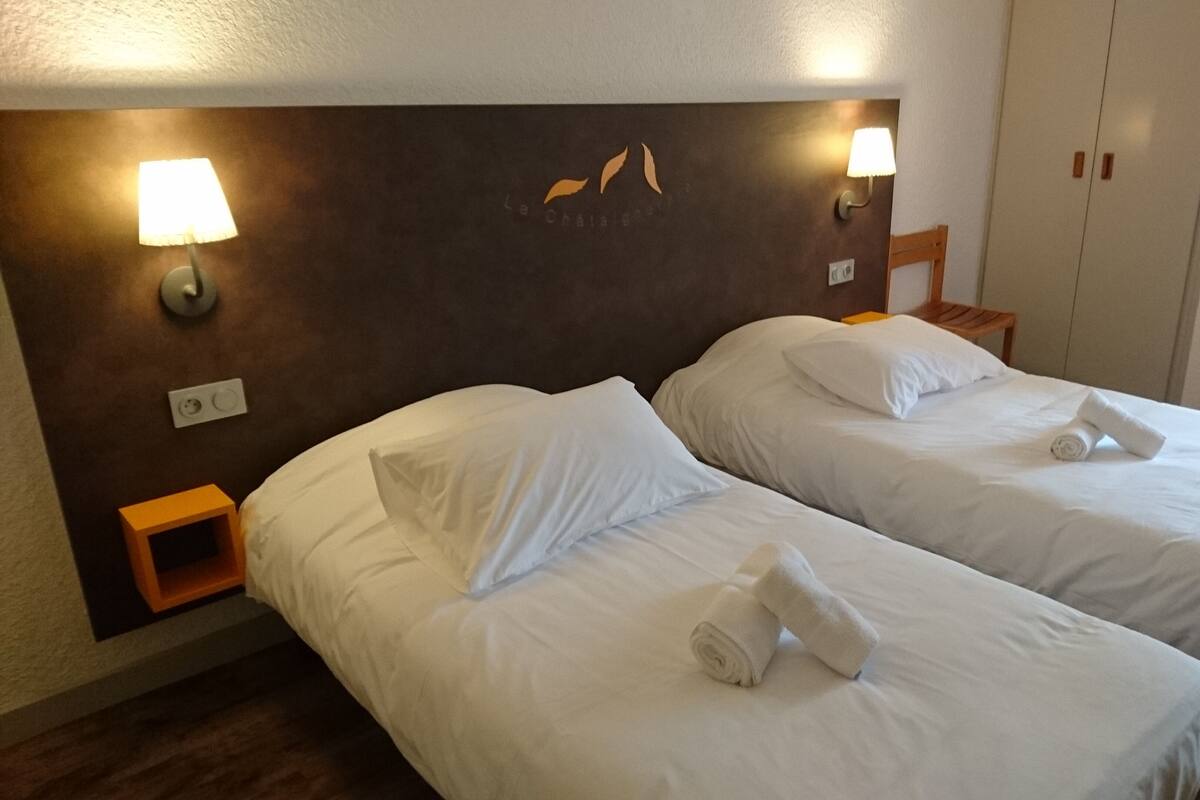 A hotel room with two beds, each with white linens and towels. There are wall-mounted lamps on either side of the beds.