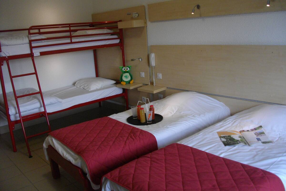 A hotel room with bunk beds, a bedside table with a lamp, a telephone, and a small shelf with a stuffed toy.