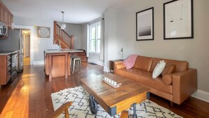 Un salon spacieux avec une table basse en bois, un canapé en cuir marron et une cuisine en arrière-plan.