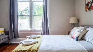 A hotel room with a bed, a nightstand, a lamp, and a window with curtains. - 2394 Indiana (SIDE) · Perfect For Groups & Families-5 Bedroom Cozy Home (Columbus)