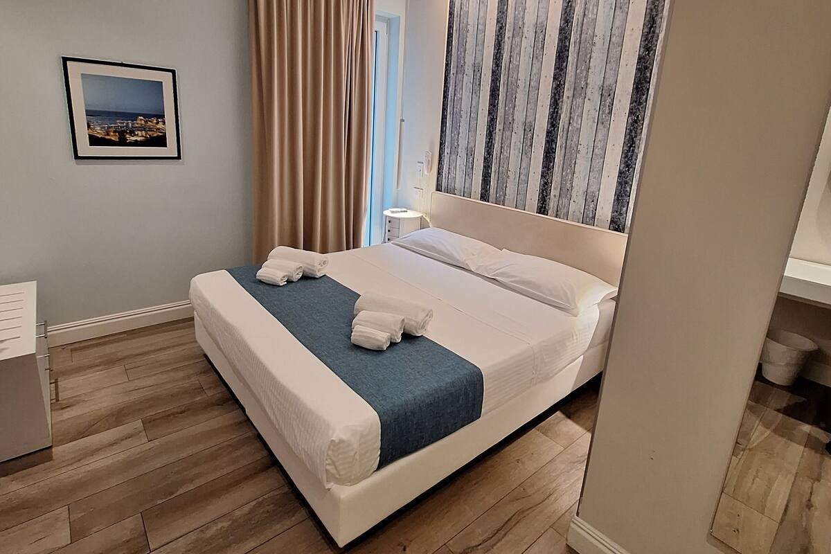 Een moderne hotelkamer met een groot bed, houten vloer, een foto aan de muur en een raam met gordijnen.