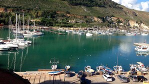 Un port de plaisance avec des bateaux amarrés, une jetée où sont garées des voitures, et un paysage vallonné en arrière-plan.