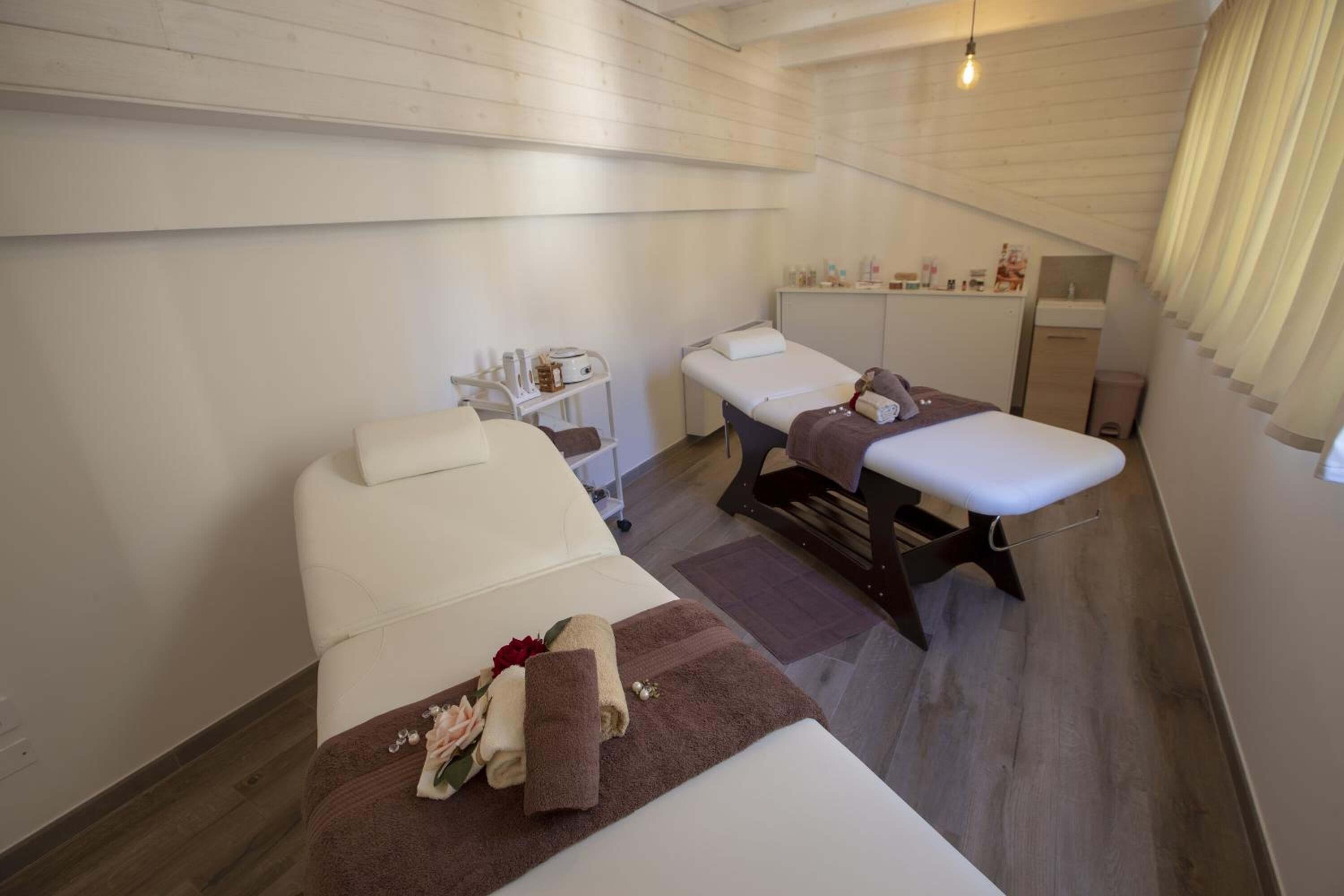 A spa room with two beds, a massage table, and a small shelf with toiletries.