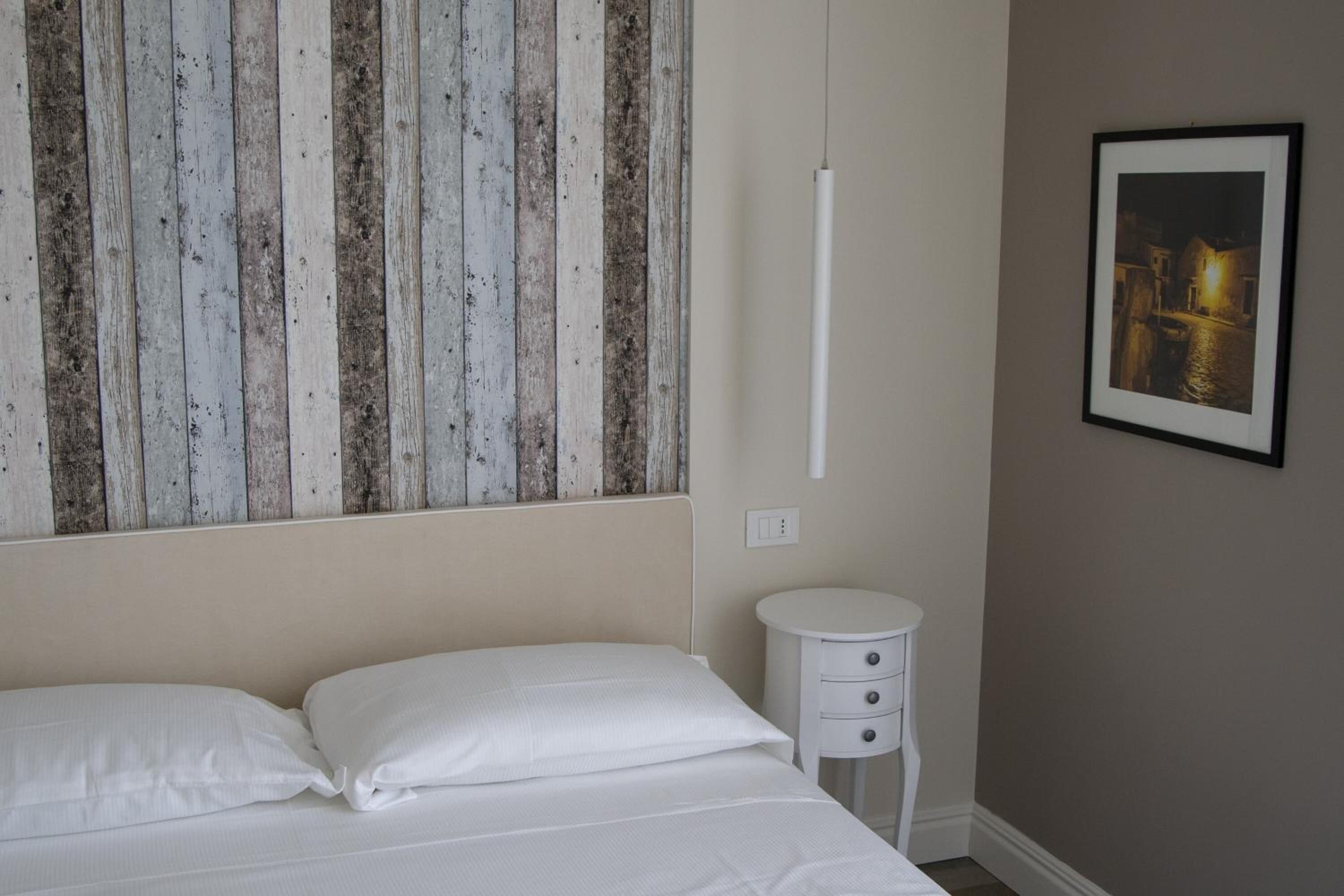 A bedroom with a bed, a nightstand, a framed picture on the wall, and a wooden panel design above the bed.