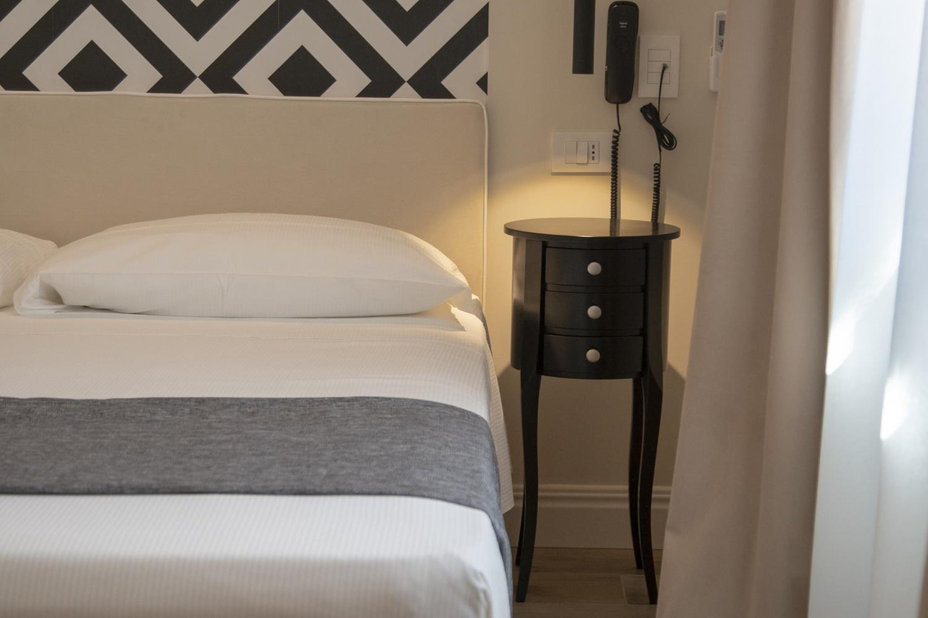 Een net opgemaakt bed met een grijze deken, een zwart-wit gestreept muur en een bedtelefoon.