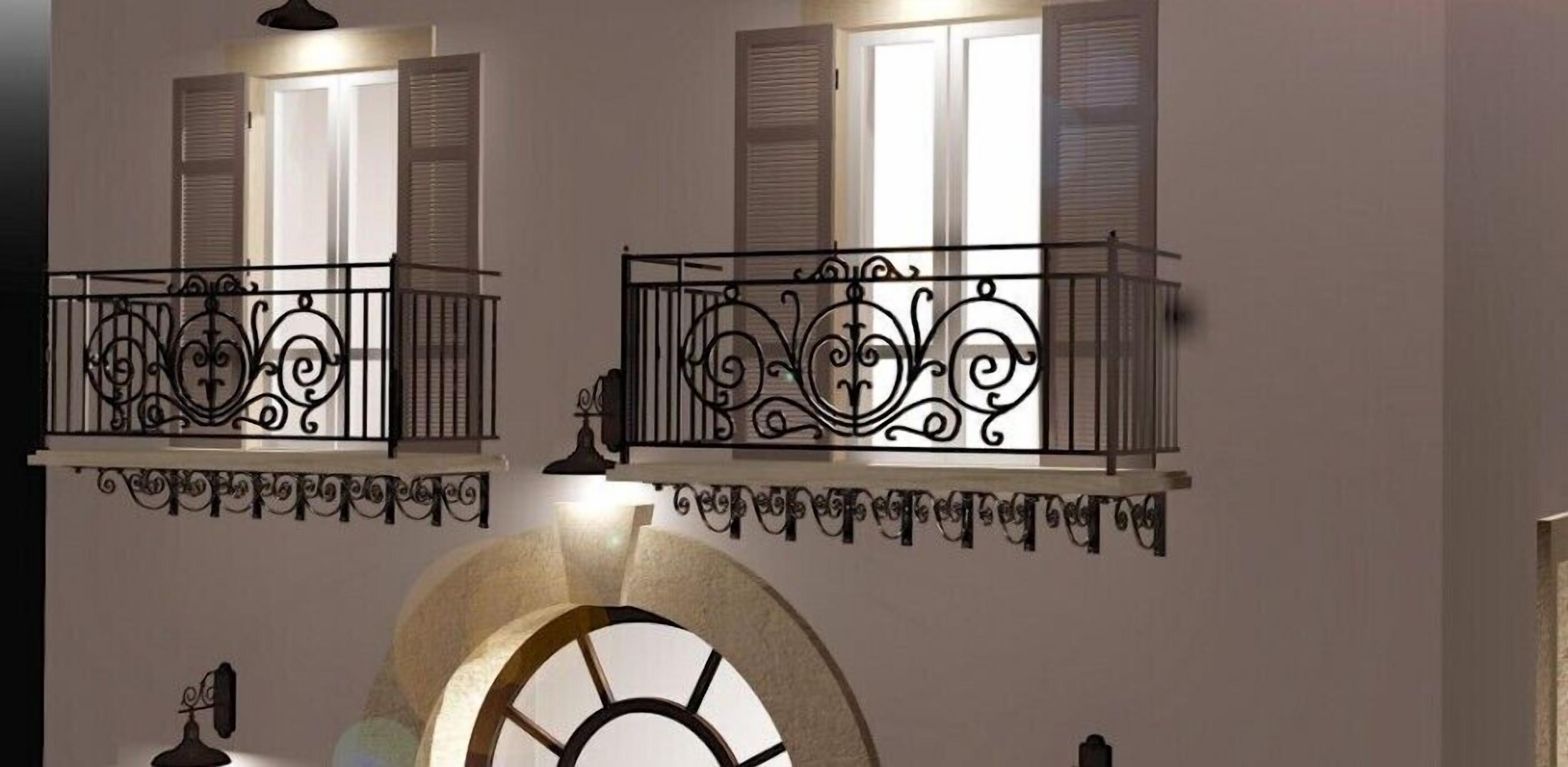 Un balcón con barandillas de metal negro ornamentado y un arco de piedra en la parte inferior.