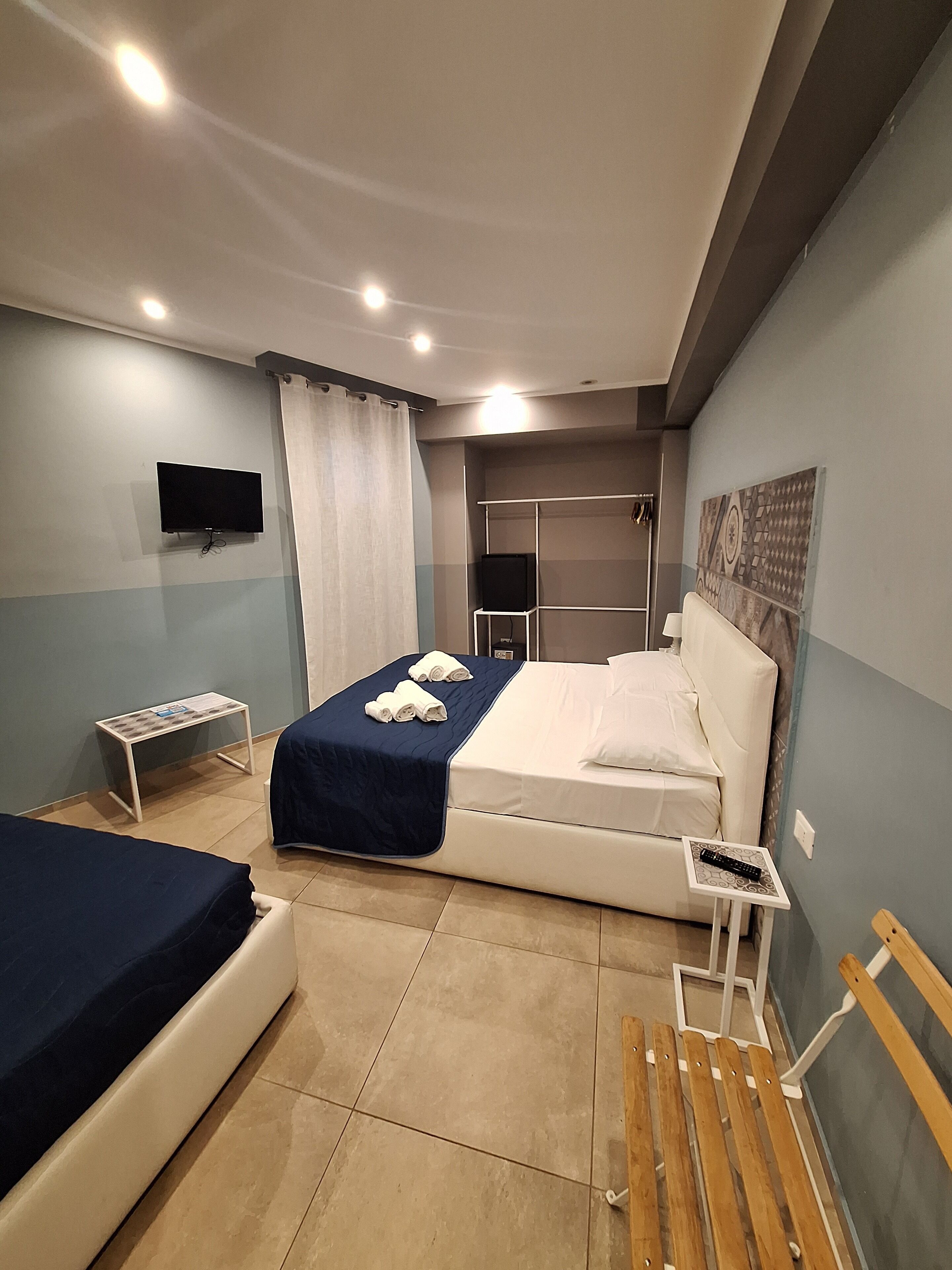 Habitación de hotel con cama, escritorio, silla, televisión y zona de ducha.