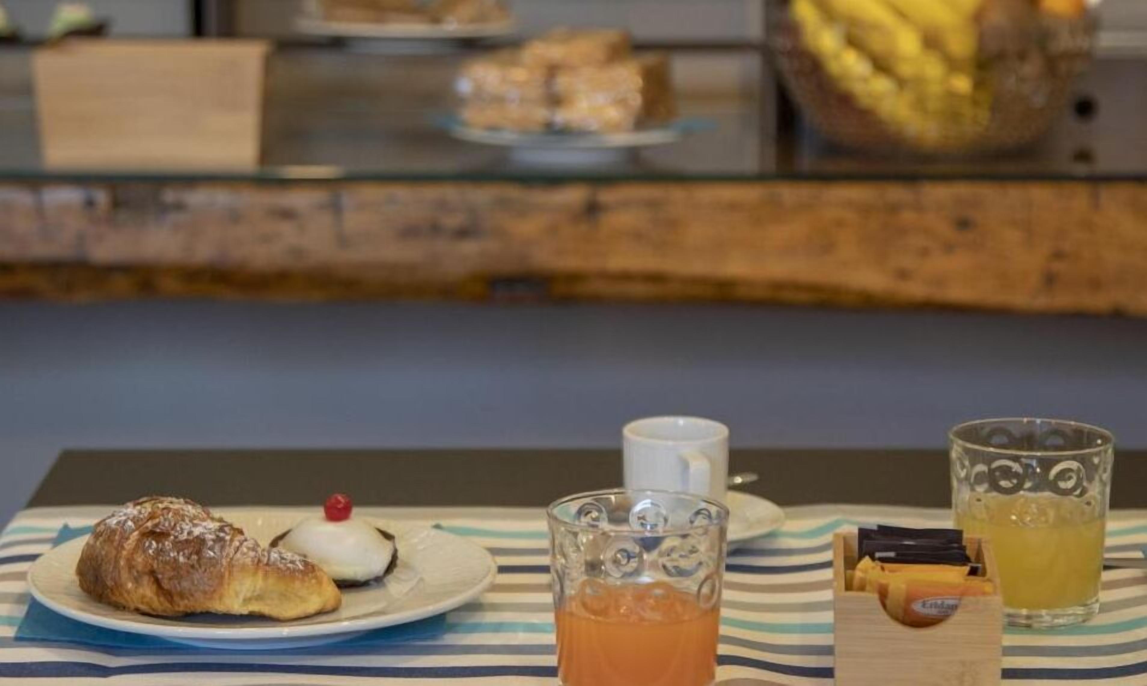 A breakfast setting with pastries, a glass of orange juice, and a cup on a striped tablecloth.