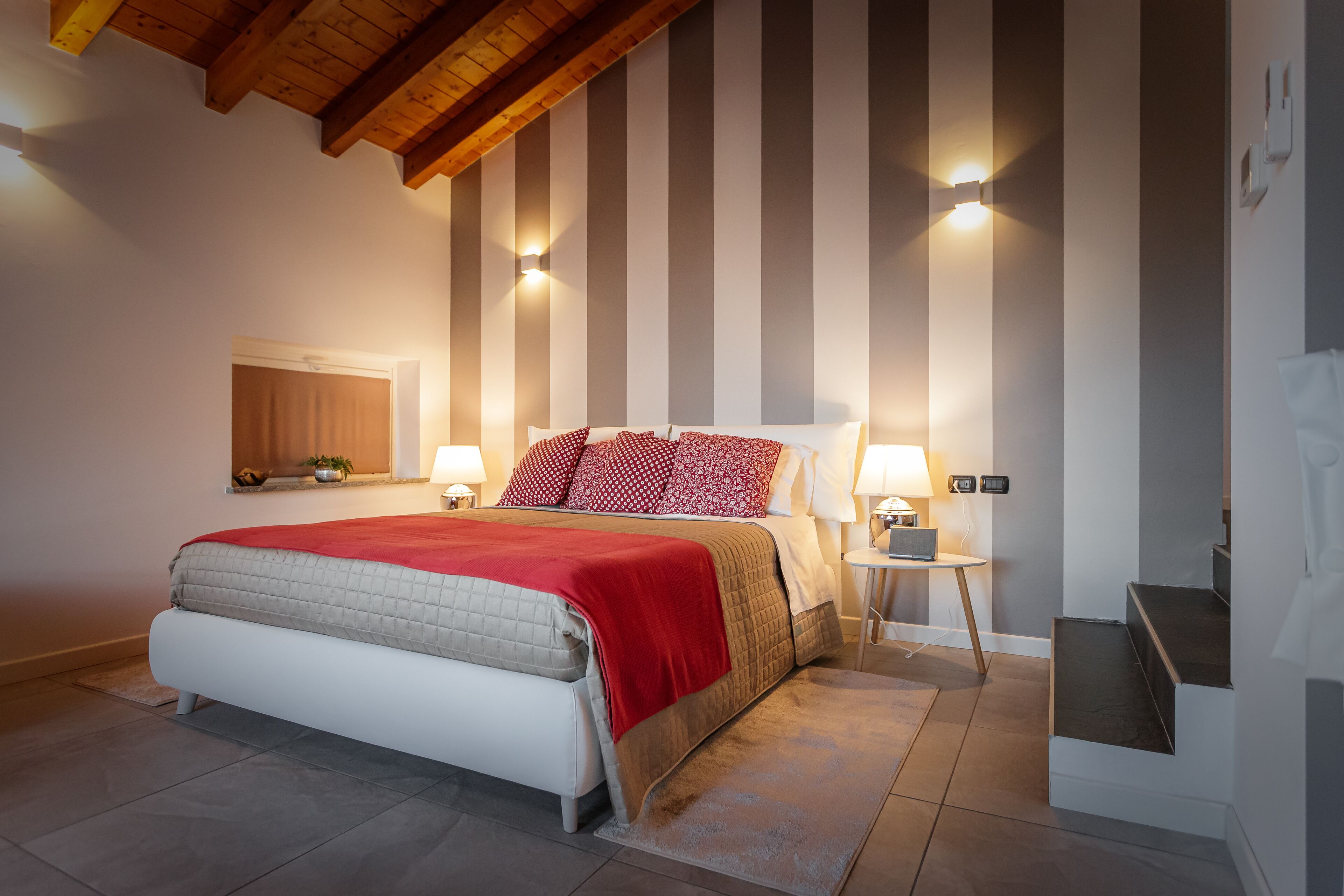 Een slaapkamer met een bed, twee nachtkastjes met lampen, een houten plafond en een trap.