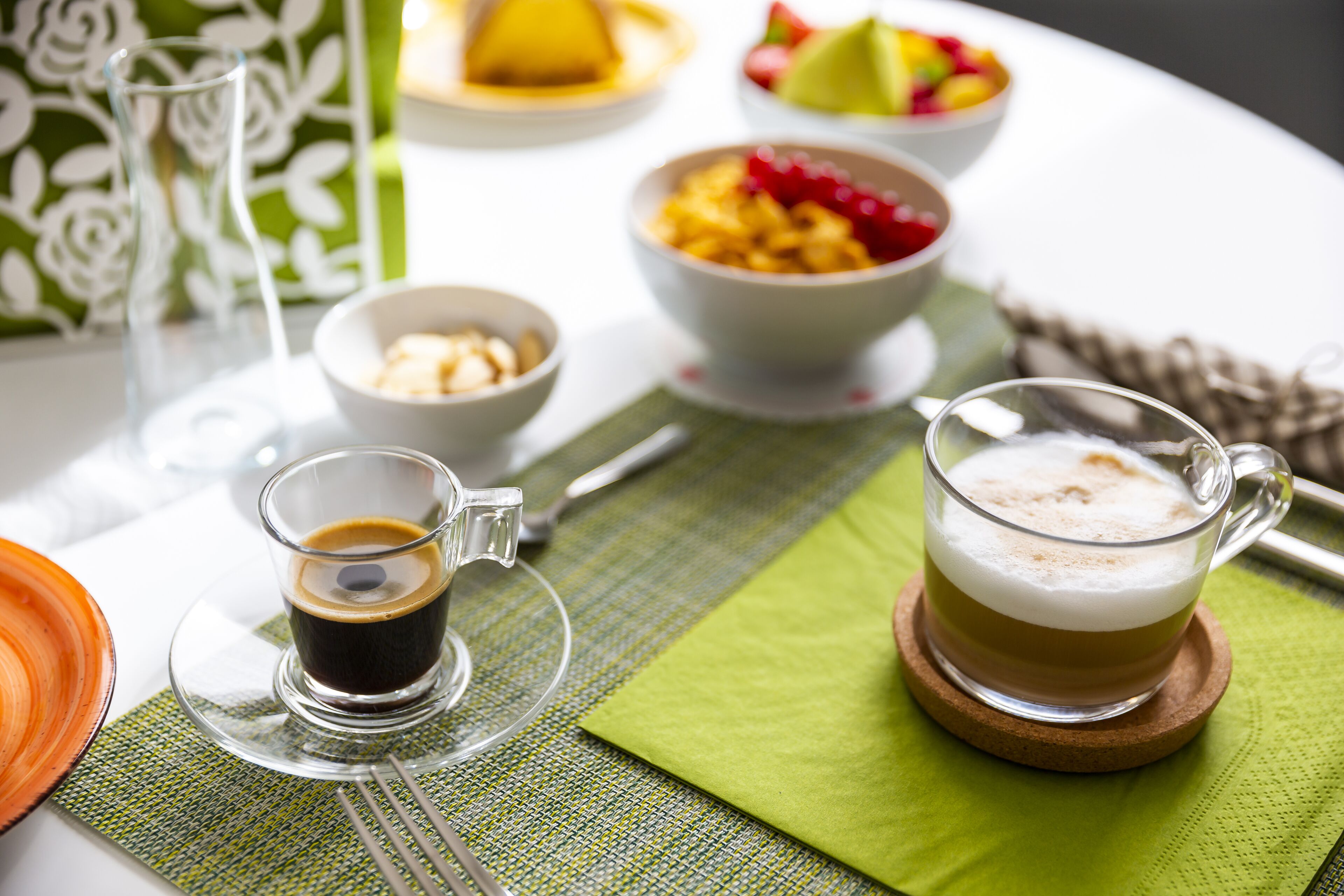 Una mesa con una taza de café, un bol de fruta y un plato de comida.