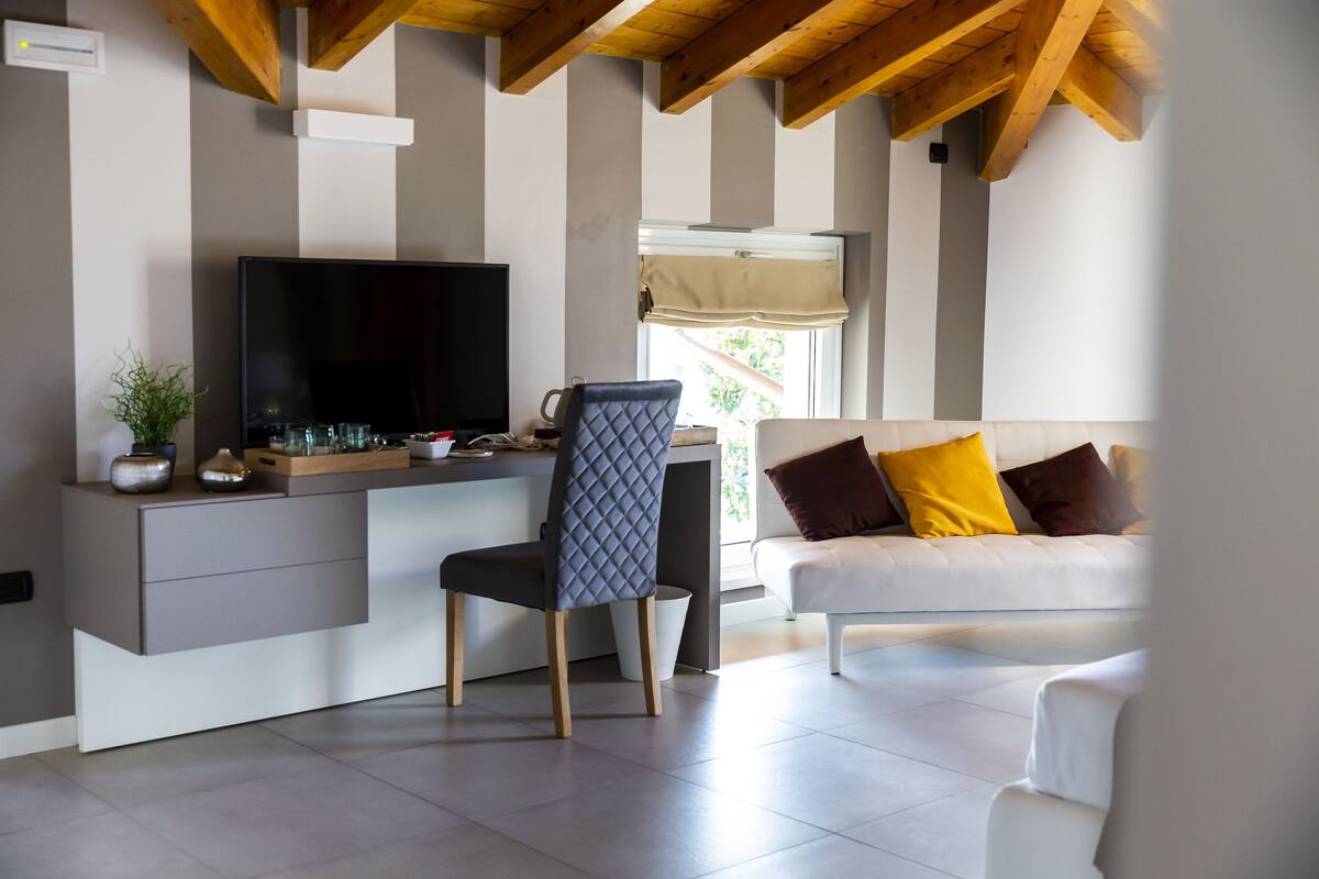 A modern living room with a flat-screen TV, a comfortable sofa with cushions, a dining area with a table and chairs, and a window with a view.