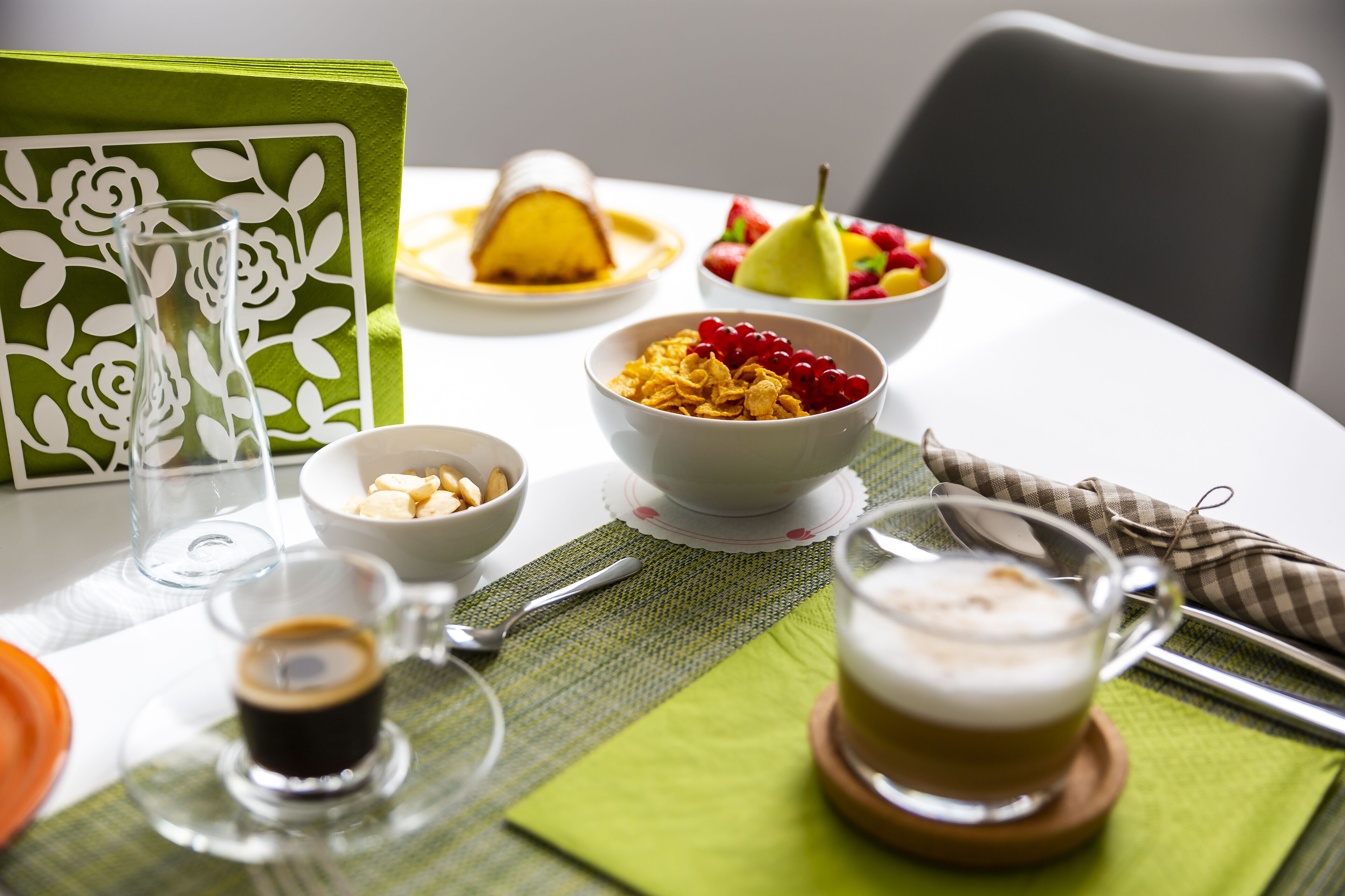 Desayuno con cereal, fruta, café y una tarjeta decorativa sobre una mesa.