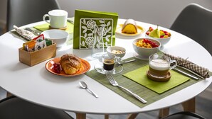Ein runder Esstisch mit verschiedenen Frühstücksangeboten, darunter ein Croissant, Kaffee und Obst.