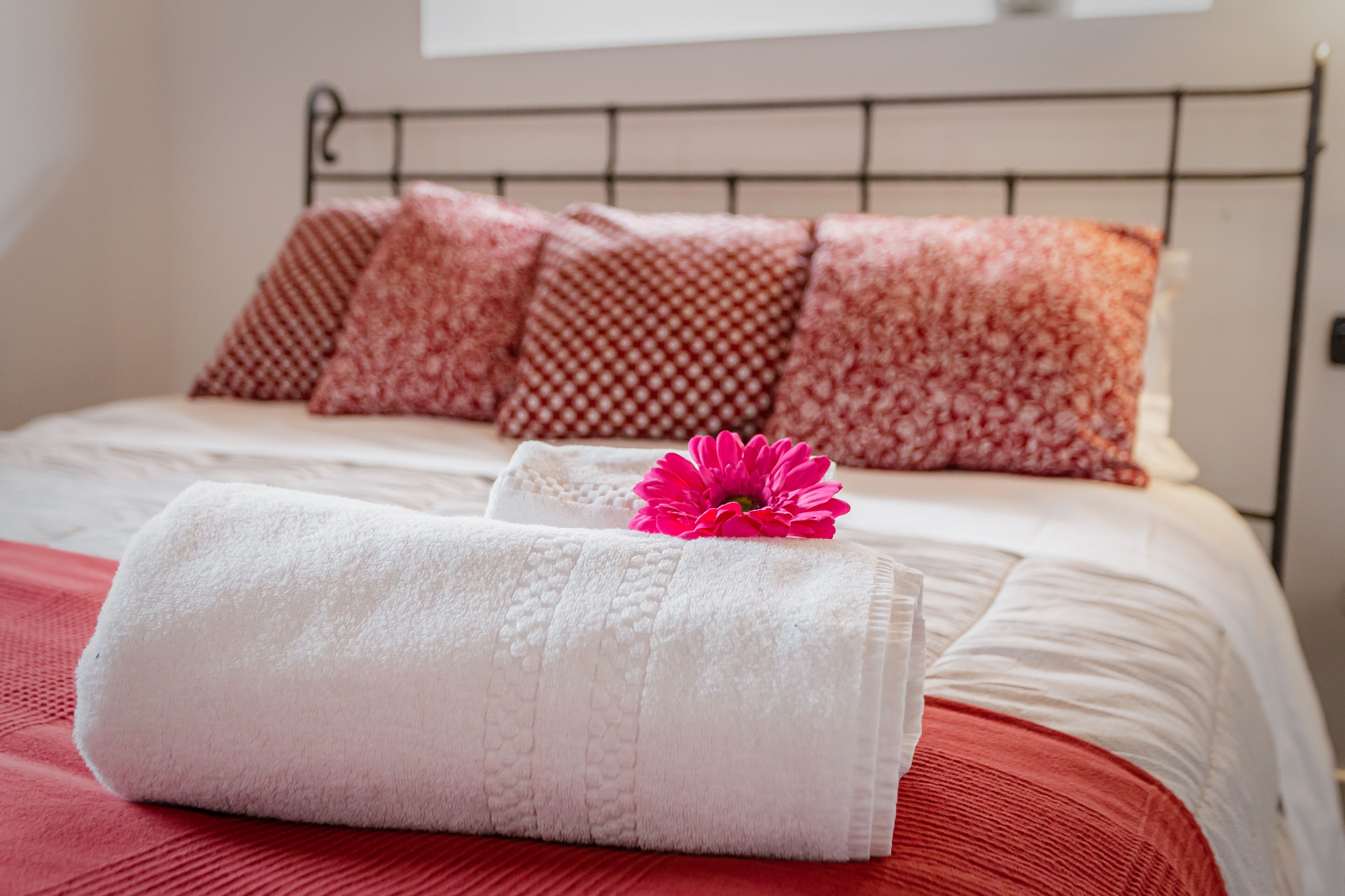 A neatly made bed with white linens, a red bedspread, and patterned pillows.