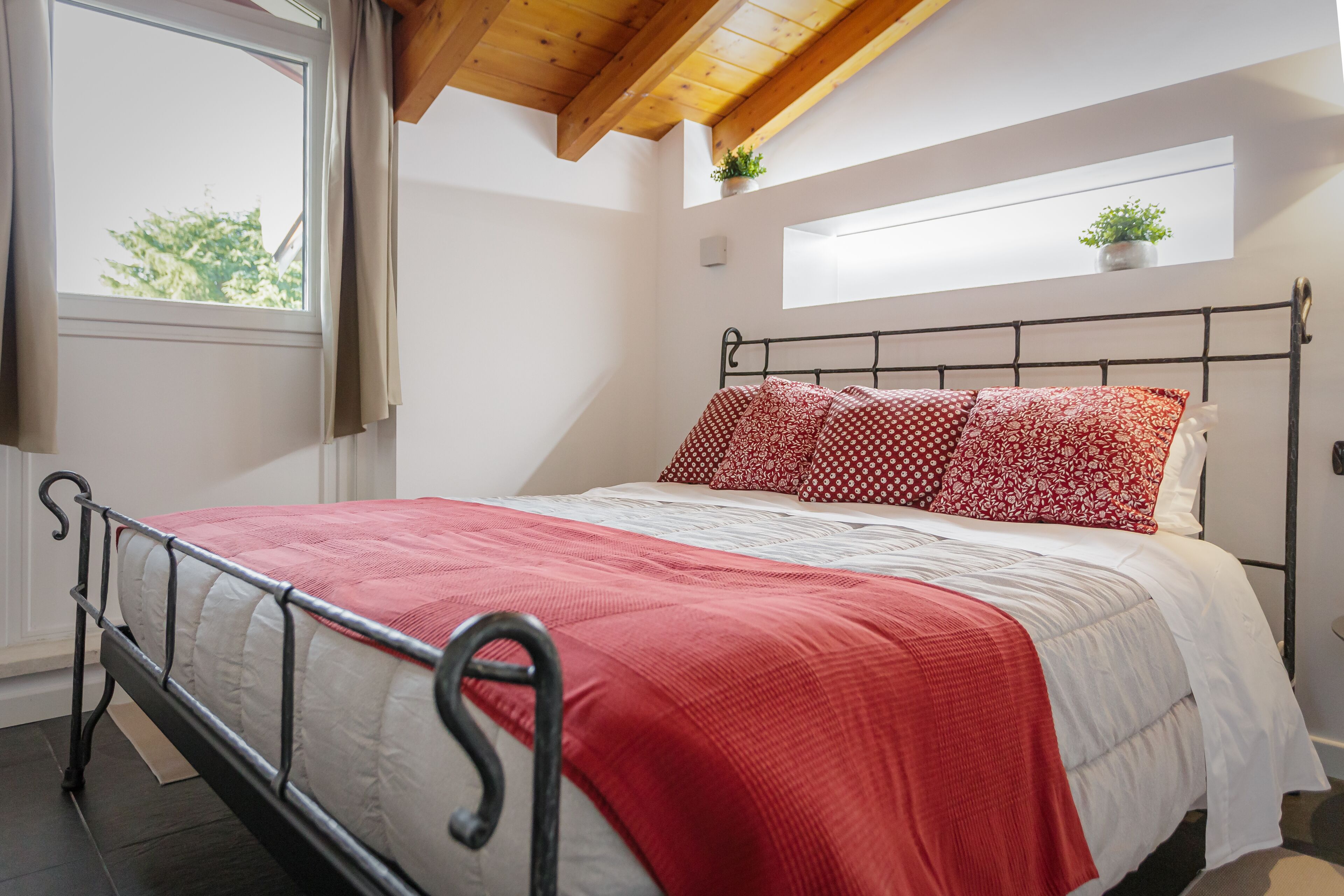 Un lit avec un cadre en métal, une couvre-lit rouge et blanche et une fenêtre avec des rideaux.