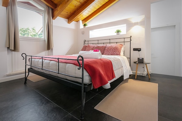 Une chambre à coucher avec un lit, une table de chevet, une fenêtre et une petite table avec une lampe.