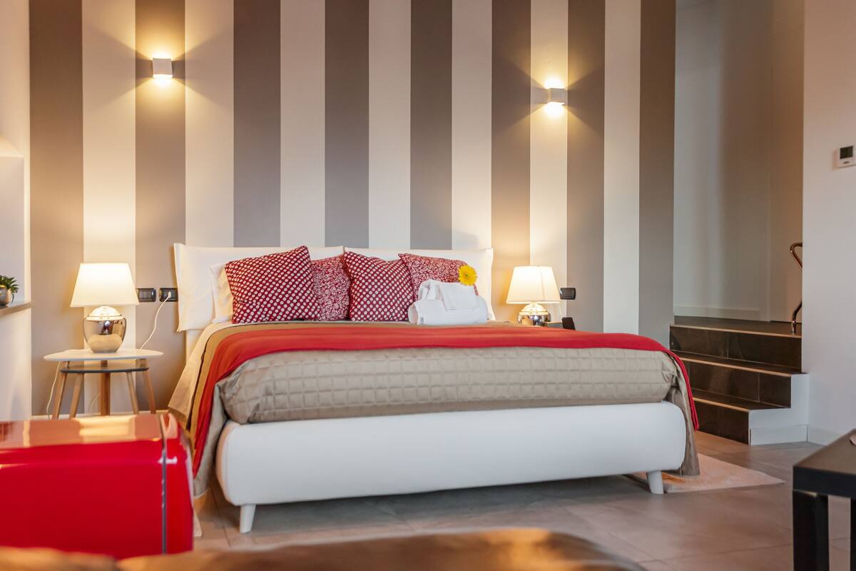 A modern bedroom with a bed, two bedside tables with lamps, a red chair, and a staircase.