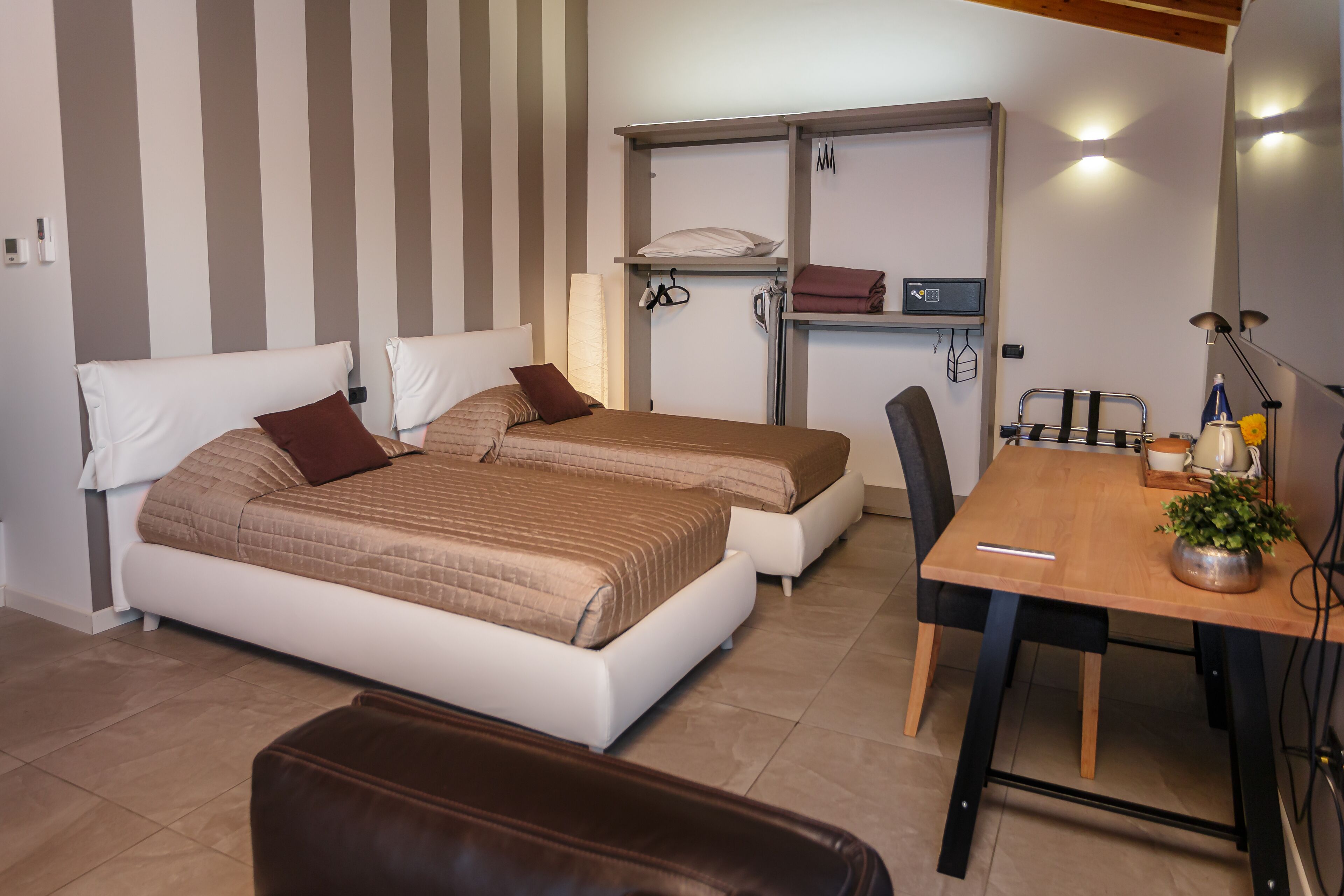 Een slaapkamer met twee bedden, een klein tafeltje en een stoel. Boven het bed bevindt zich een plank met opgevouwen kleding en een lamp.
