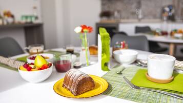 Una colazione con una ciotola di frutta, uno stampo dolce, una tazza di caffè e un vaso con fiori.