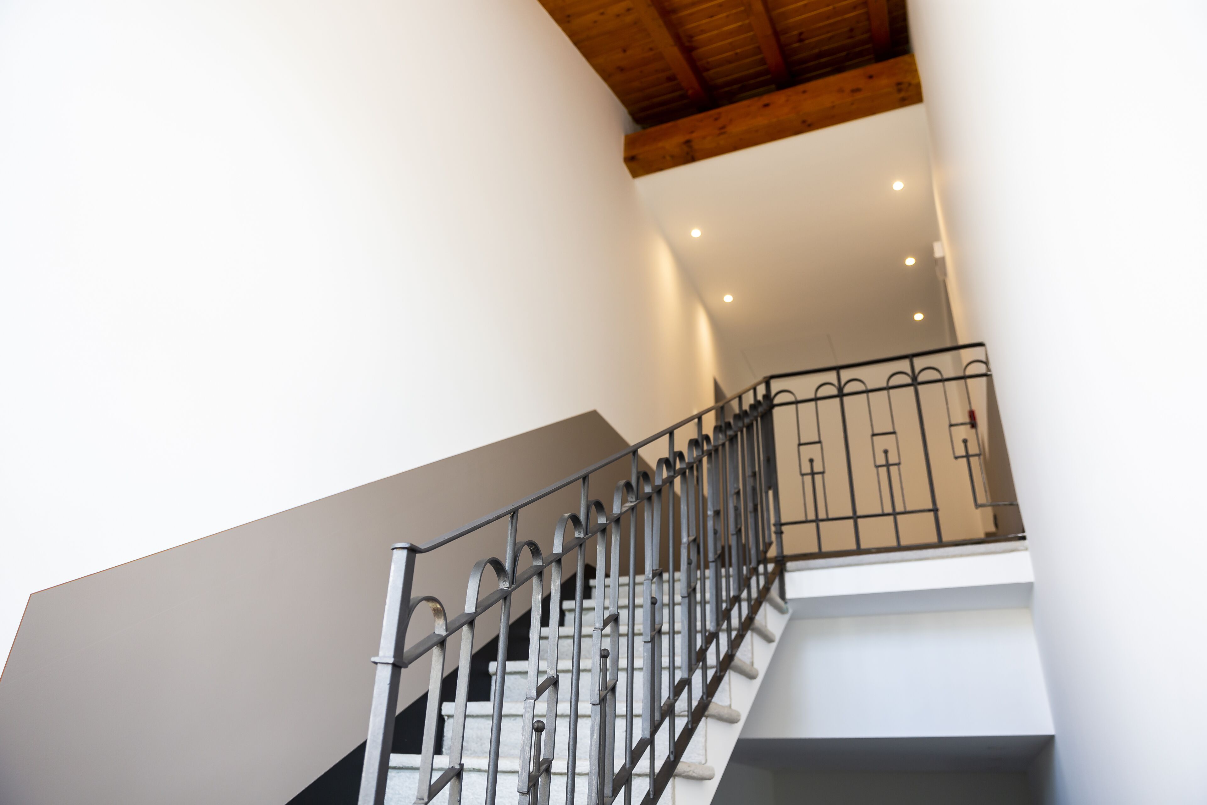 Una scala con ringhiera in metallo, travi del soffitto in legno e illuminazione a incasso.