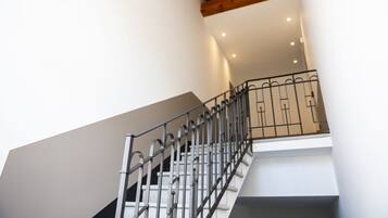 Una scala con ringhiera in metallo, travi del soffitto in legno e illuminazione a incasso.