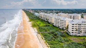 Un hotel frente a la playa con varias construcciones, una playa arenosa y vista al océano.