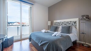 Ein Hotelzimmer mit Bett, Schreibtisch, Stuhl, Lampe und Blick auf die Stadt durch ein großes Fenster.