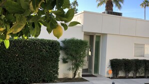 Un edificio moderno con un césped cuidado, un seto y una palmera al fondo.