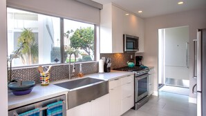 Una cocina moderna con una isla grande, electrodomésticos de acero inoxidable y vistas a palmeras afuera.