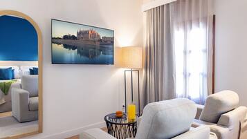 Une chambre d’hôtel moderne avec un grand miroir, un canapé confortable, une petite table avec une lampe et un tableau représentant un paysage urbain accroché au mur.