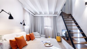 Une chambre d’hôtel moderne avec un lit, un bureau, une valise et un escalier.