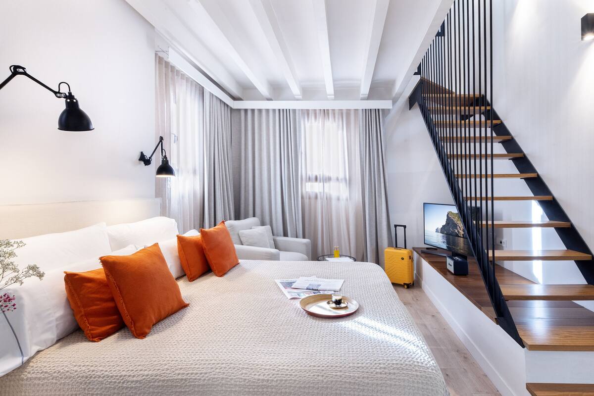 Une chambre d’hôtel moderne avec un lit, un bureau, une valise et un escalier.