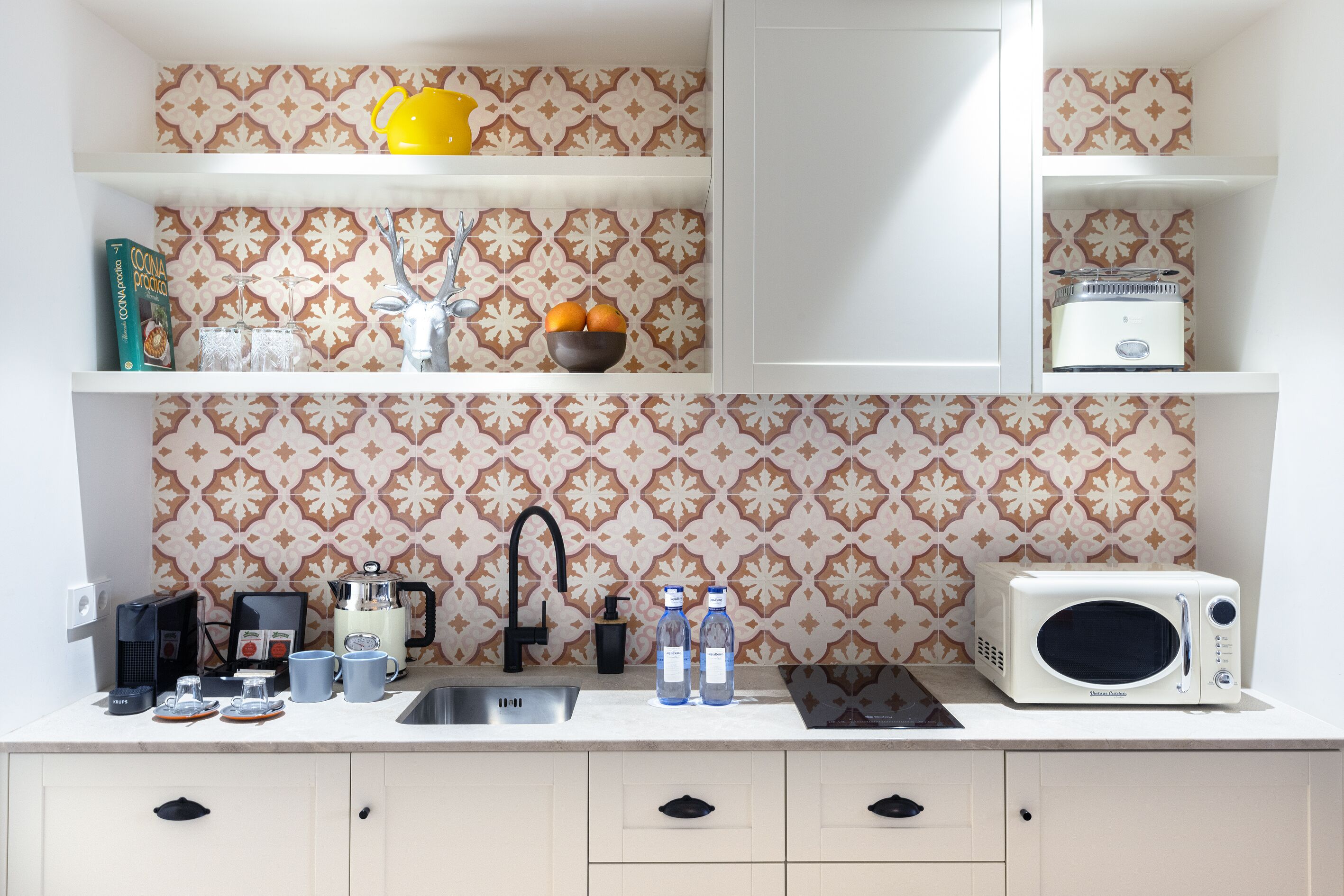 Una cocina con salpicadero decorado, cafetera, microondas y pileta.
