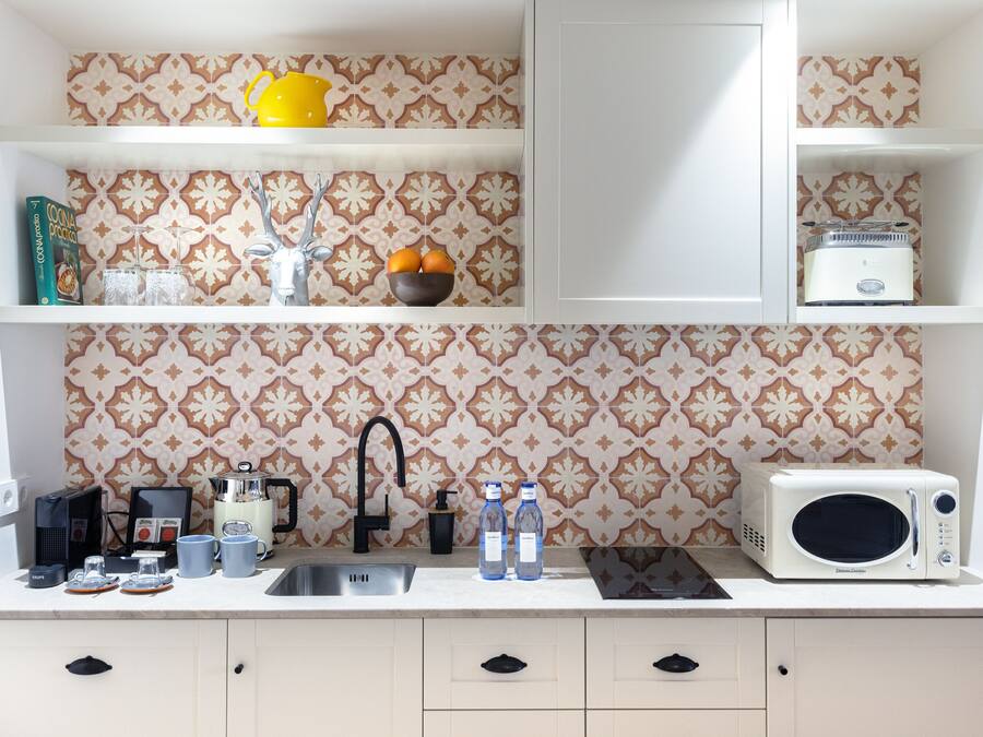 A kitchen with a patterned backsplash, a coffee maker, a microwave, and a sink.