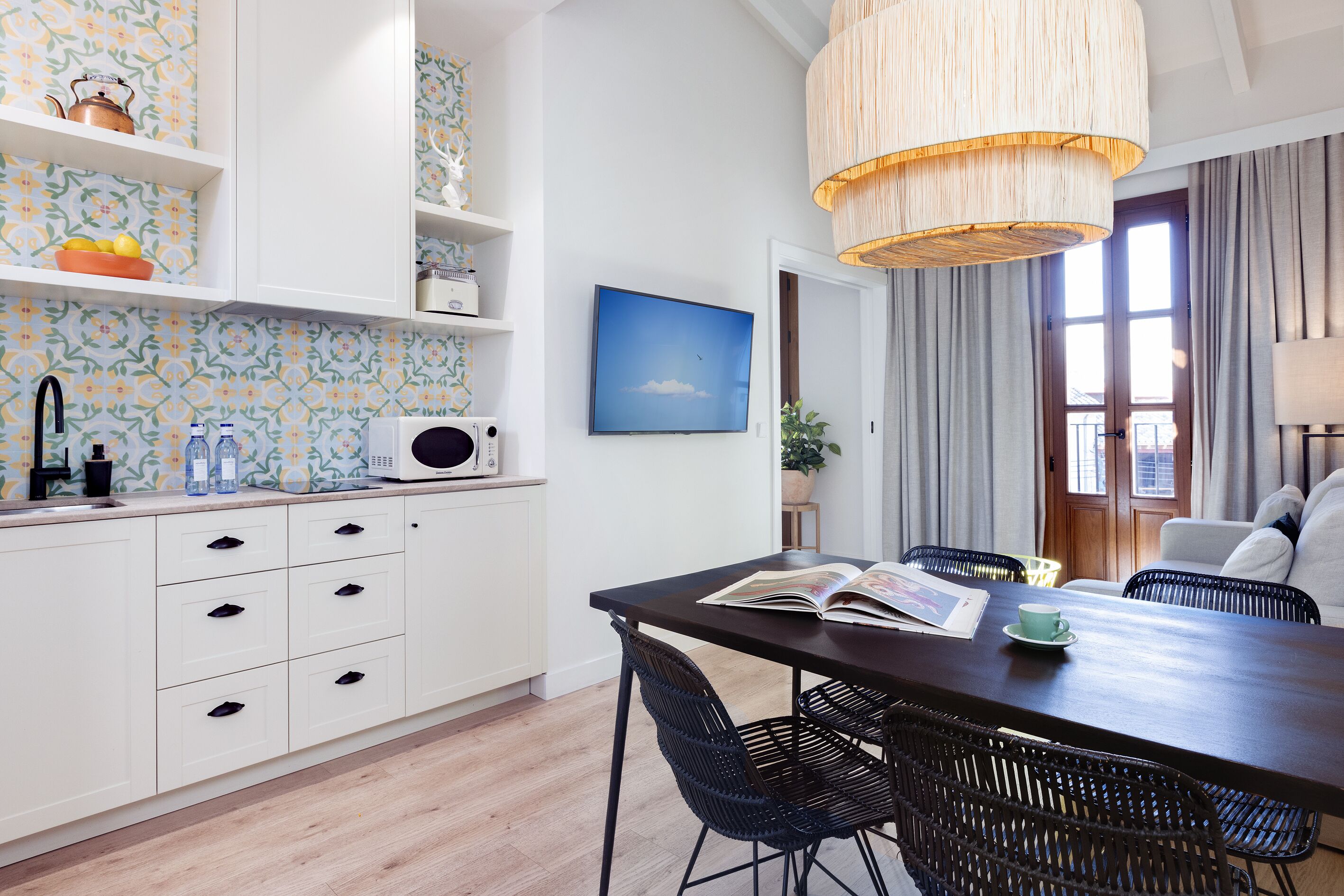 Una cocina moderna con armarios blancos, un microondas y una zona de comedor con mesa y sillas.