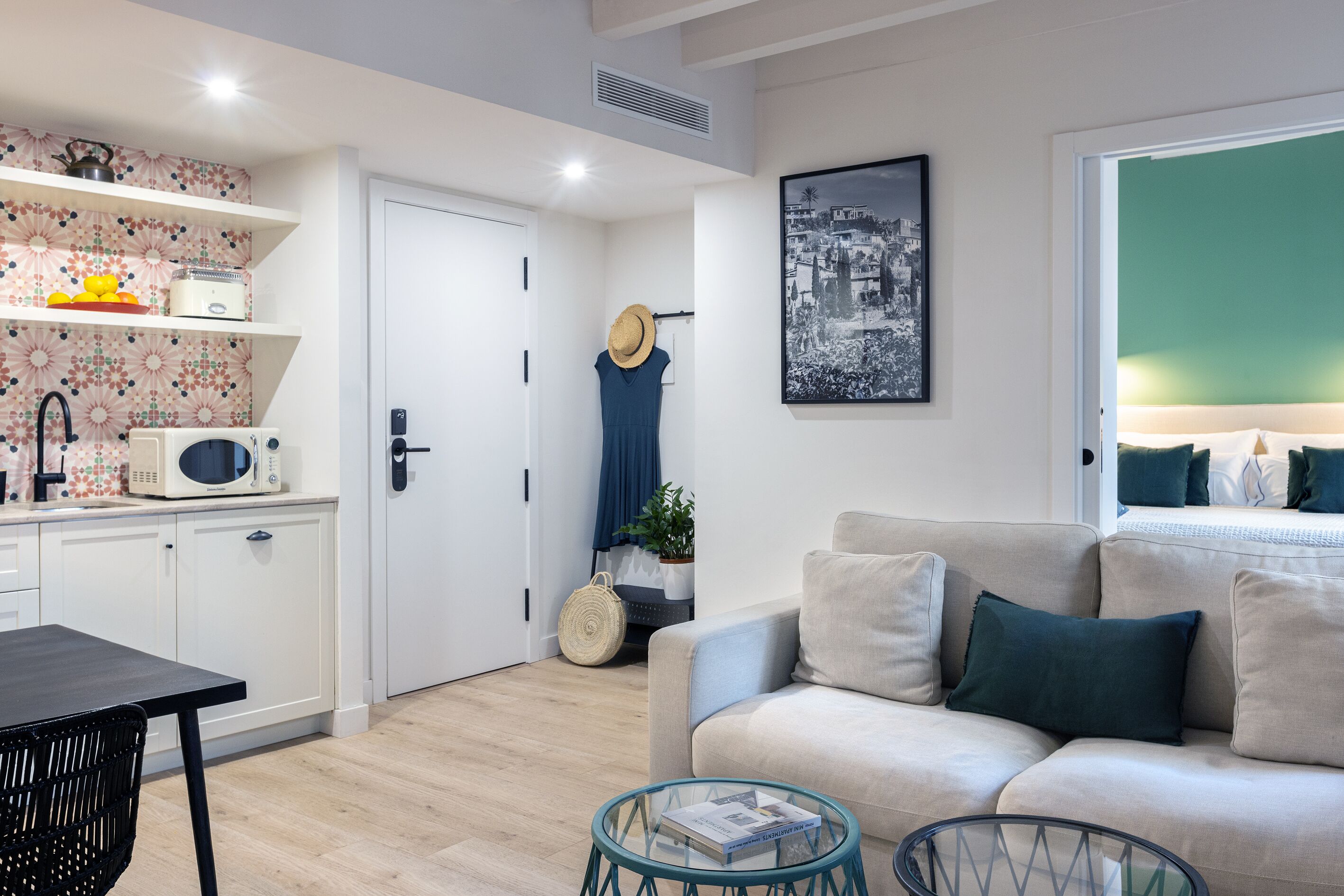 A modern living room with a sofa, a glass coffee table, a kitchen area with a microwave, and a dining table.