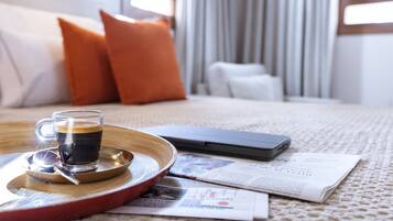 Habitación de hotel ordenada con cama, mesita de noche, taza de café, teléfono inteligente y periódicos.