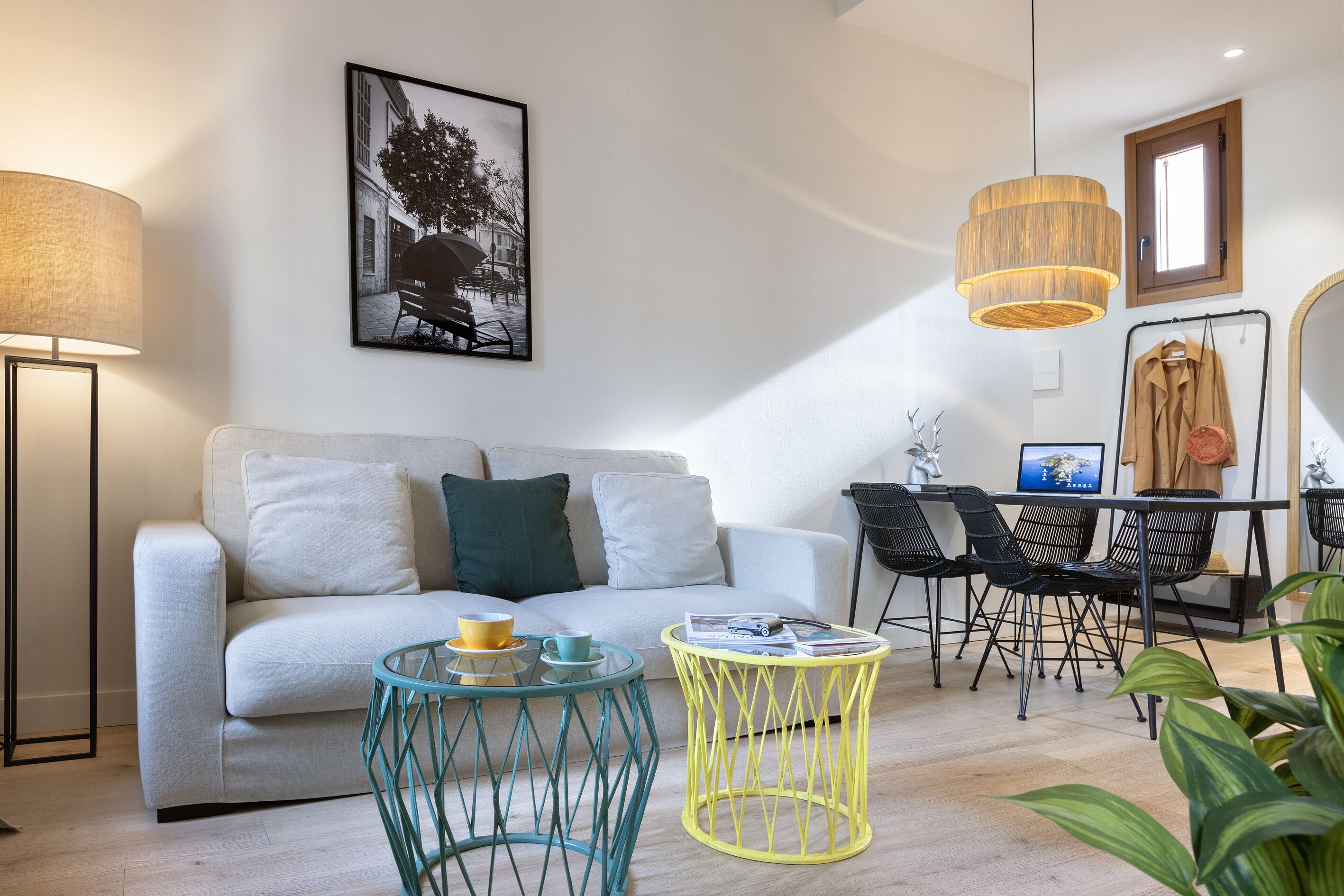A modern living room with a sofa, two coffee tables, a dining area with chairs, and a hanging light fixture.