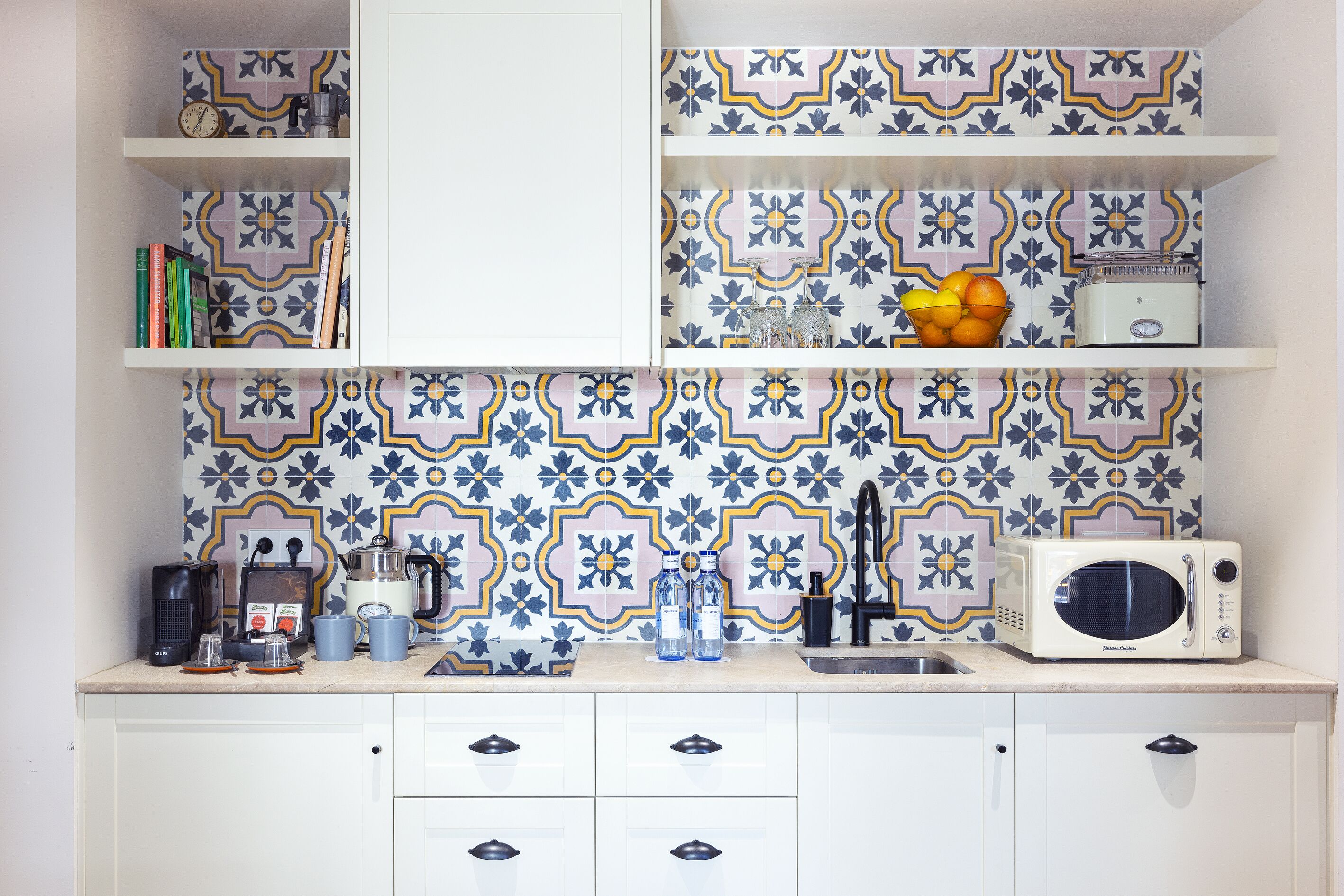 Een keuken met witte kasten, een magnetron, een koffiezetapparaat en een spoelbak.