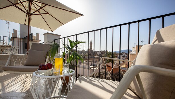 Ein Balkon mit einem weißen Stuhl, einem Tisch mit einem Getränk und Blick auf Gebäude.