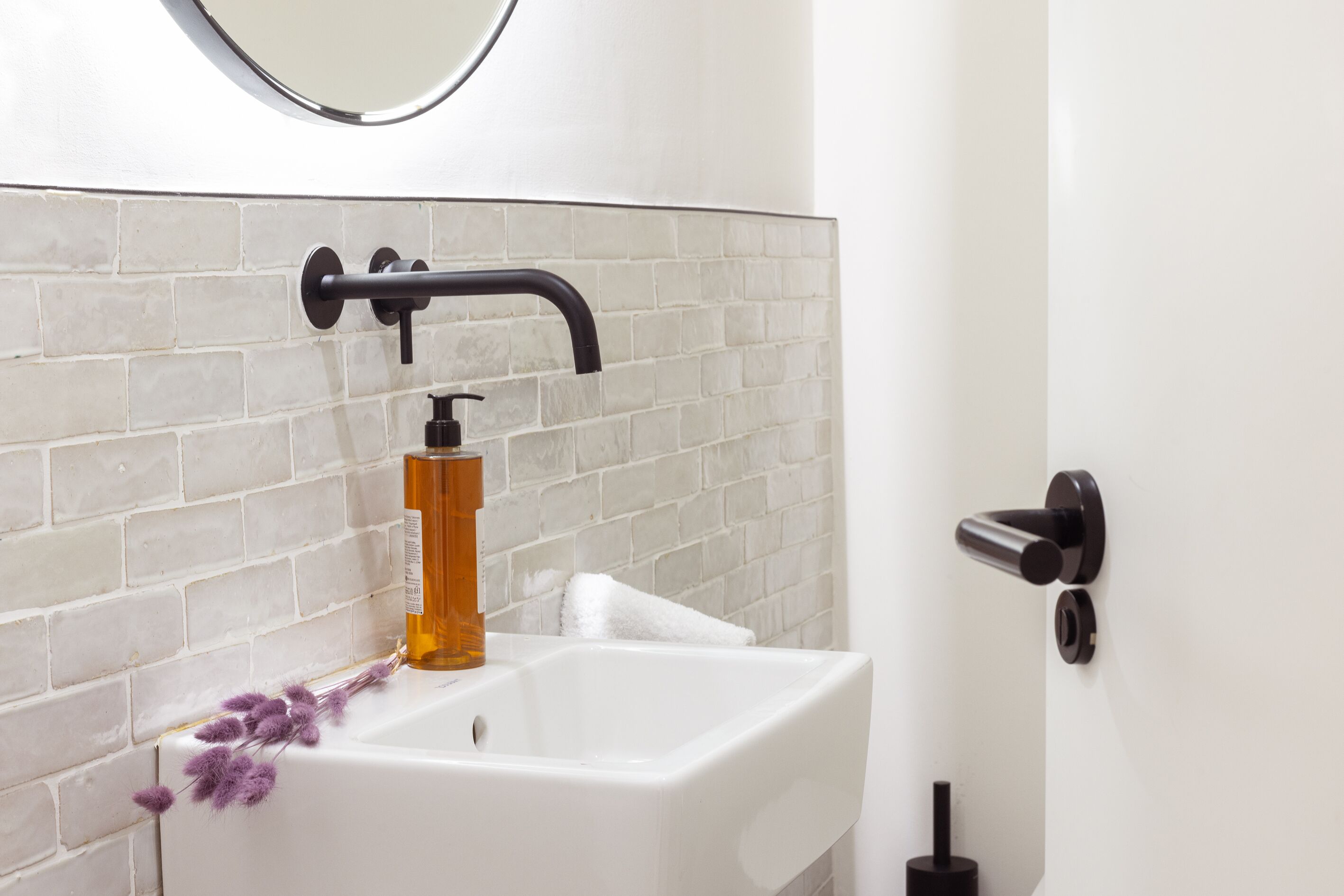 A bathroom with a white sink, a black faucet, and a bottle of soap.