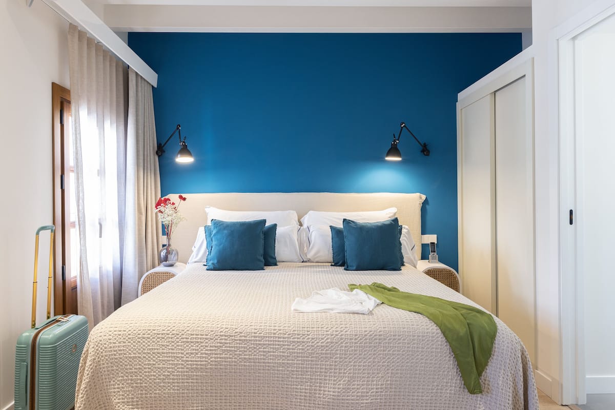 Une chambre à coucher avec un lit, deux lampes de chevet, une valise et une fenêtre avec des rideaux.