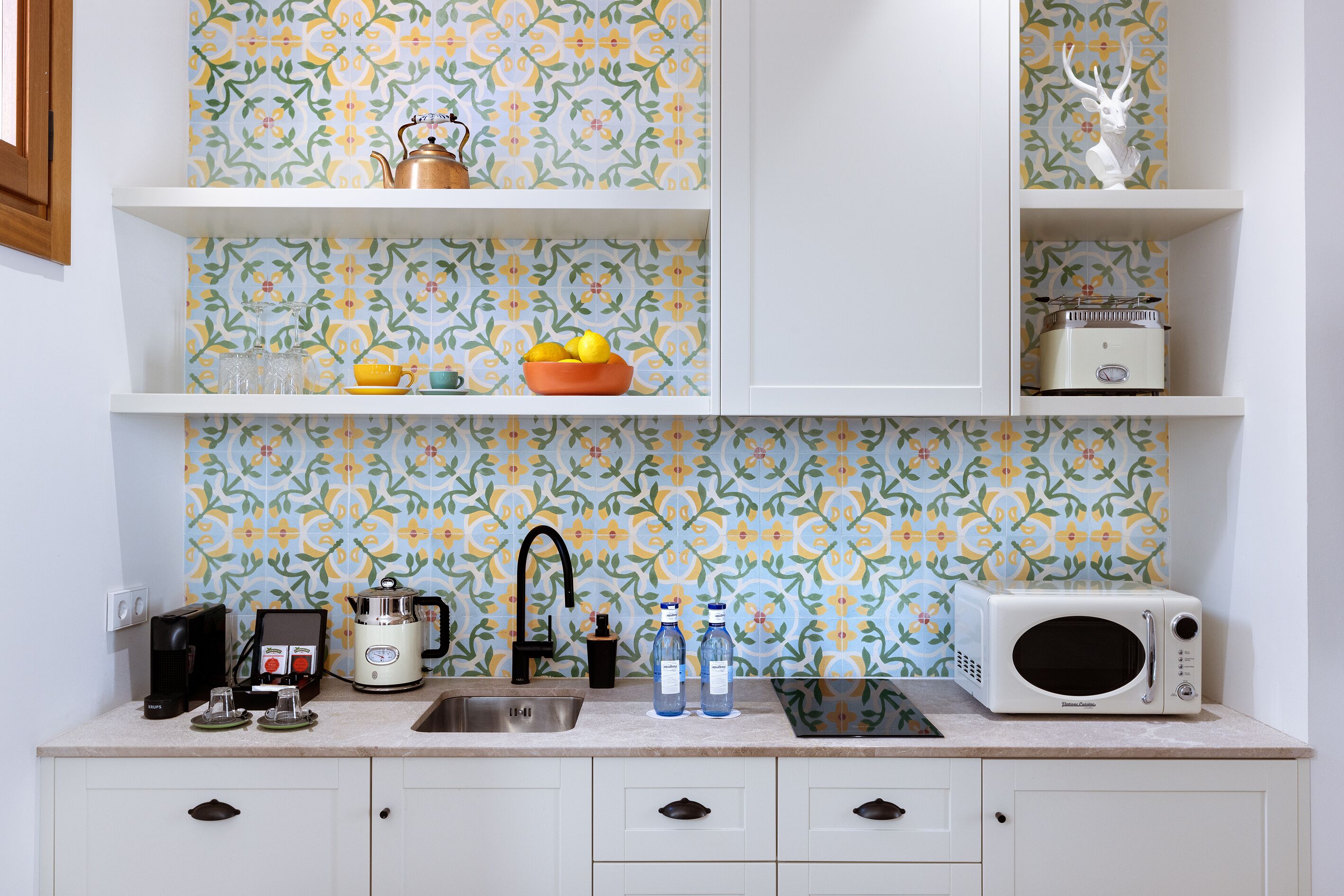 A kitchen with white cabinets, a sink, a coffee maker, a kettle, and a microwave.