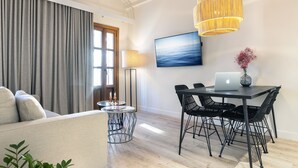 Ein modernes Wohnzimmer mit einer Couch, einem Esstisch und Stühlen. Auf dem Tisch steht ein Laptop, eine Lampe und an der Wand hängt ein Gemälde.