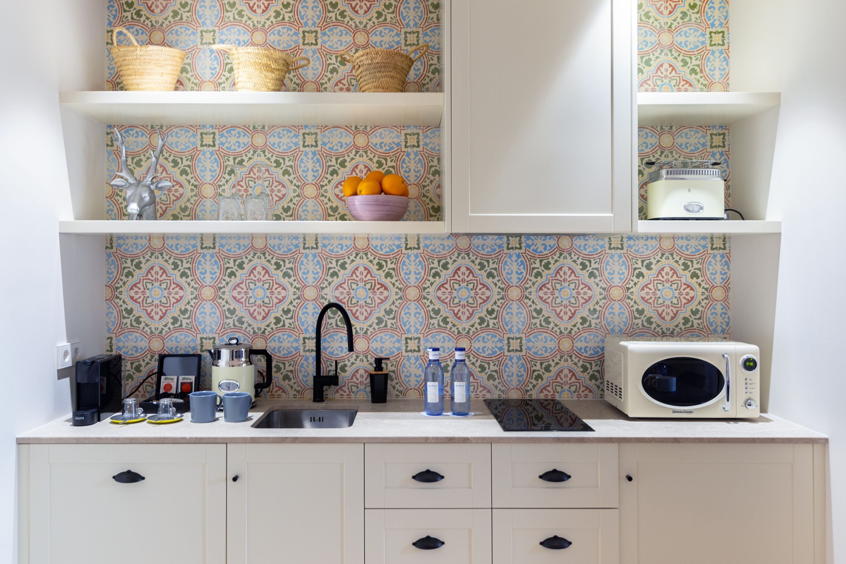 Una cocina con armarios blancos, un salpicadero estampado y un microondas en la encimera.