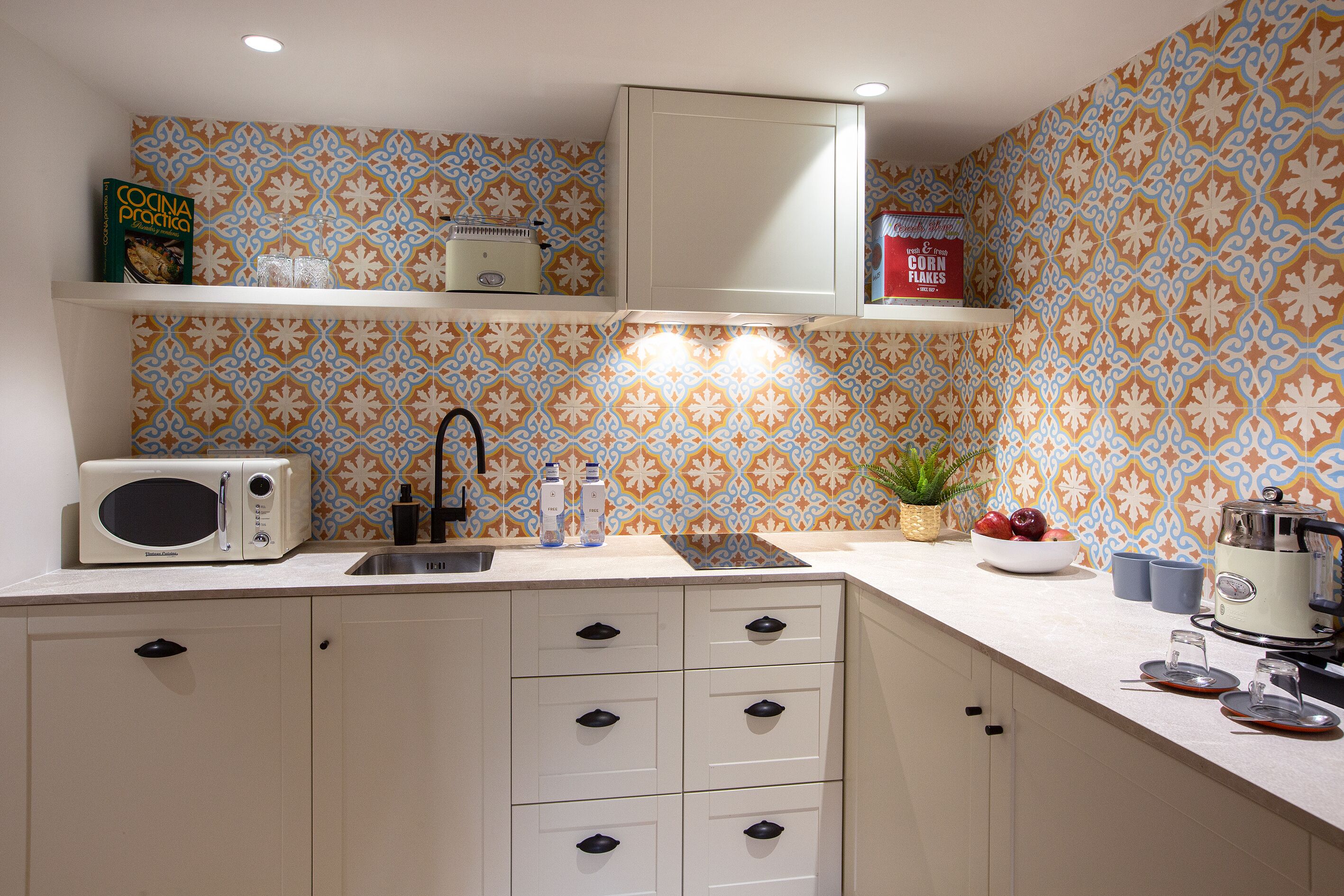 Una cocina con salpicadero estampado, armarios blancos, microondas, fregadero y estufa.