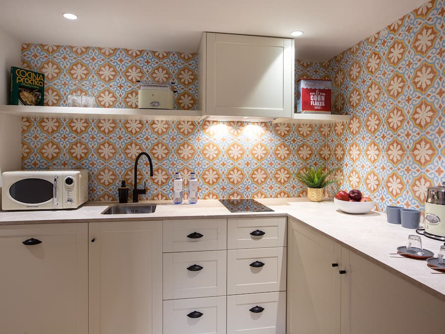 Una cocina con salpicadero estampado, armarios blancos, microondas, fregadero y estufa.