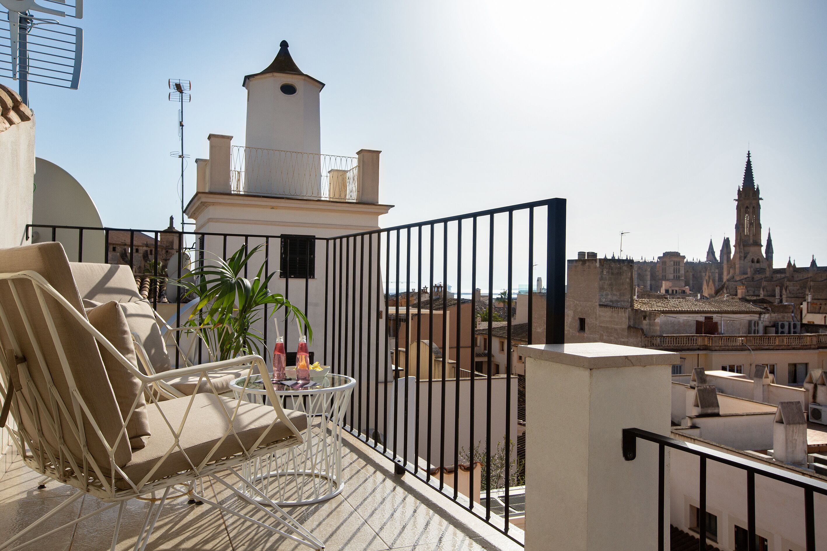 Ein Balkon mit weißem Stuhl und Tisch, einem Blumentopf und Blick auf historische Gebäude und einen Turm.